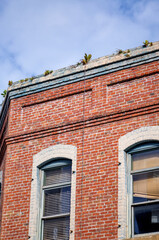 Fototapeta premium Old Red Brick Building with Green Plants Growing on the Roof.