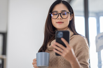 Asian businesswoman uses a mobile phone in her private Project stats financial data sales charts on laptop in office and smiles happily.