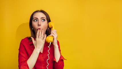 Portrait photo of an emotionally surprised girl holding a retro yellow telephone receiver and talking in isolation against a bright yellow background. A place for your text. - obrazy, fototapety, plakaty
