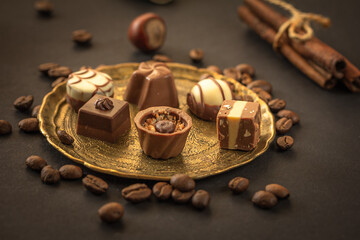 Gourmet chocolates, pralines, nuts, coffee beans on vintage metallic plate on dark , copy space