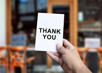 hand holding card with the word thank you. in front of coffee shop background