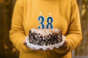 Woman holding a delicious cake with number 38 candles while celebrating birthday party. Birthday...
