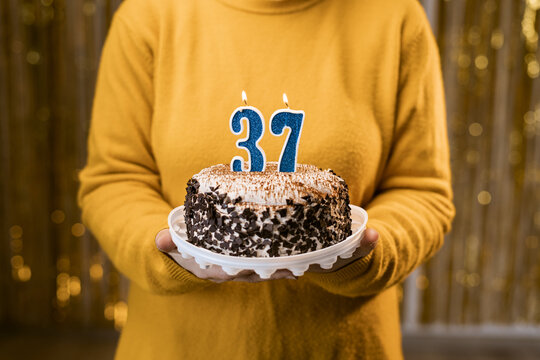 Woman holding a delicious cake with number 37 candles while celebrating birthday party. Birthday holiday party people concept.