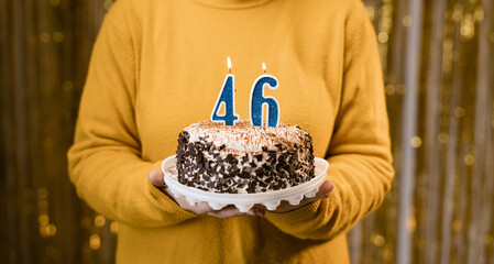 Woman holding a delicious cake with number 46 candles while celebrating birthday party. Birthday holiday party people concept.