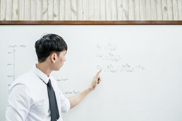 Fototapeta premium An Asian male teacher in a classroom near the whiteboard is writing and teaching a lesson with a special lecture in a class column. Math teacher explains arithmetic sums to university students