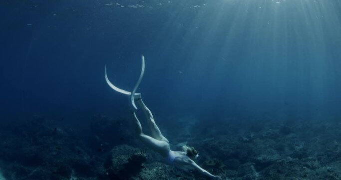 Freediver girl with fins glides underwater in transparent ocean. Freediving water sport in tropical blue sea.