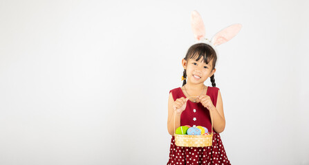 Happy Easter Day. Smile Asian little girl wearing easter bunny ears holding basket of full colorful eggs smiles broadly isolated on white background with copy space, Happy child in holiday