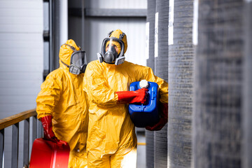 Fully protected workers in yellow hazmat suit, gas masks and gloves handling dangerous chemicals or substances.