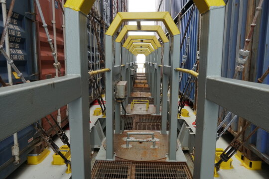 Cross deck protected by metal constructions on the container vessel. Catwalk  in diminish perspective passing between rows of lashed containers from different colors.