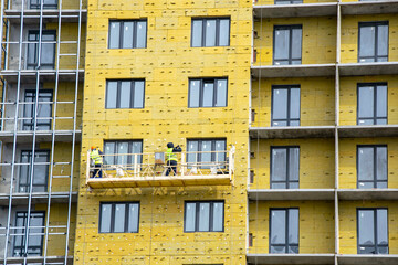 workers at the construction elevator insulate the facade of the building