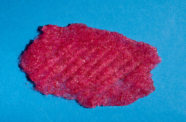 Smear of pink skin scrub close-up on a blue background.