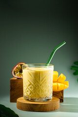 Mango, banana, passion fruit and coconut smoothie. Tropical yellow mocktail in a glass with green...