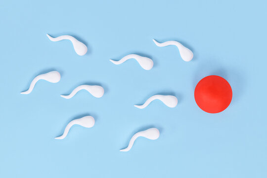 Abstract sperm cells swimming towards egg cell on blue background