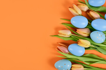 Tulip spring flowers and blue Easter eggs on side of orange background with copy space