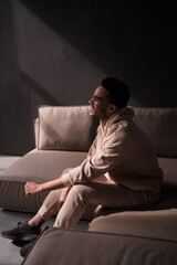 Fototapeta na wymiar Stylish African American man wearing black framed glasses on a sofa in minimalistic interior