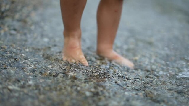 Child feet walking at shore with feeling gravel rocks shore in super slow motion 240 fps. Little boy walks outdoors. Kid lifestyle vacations