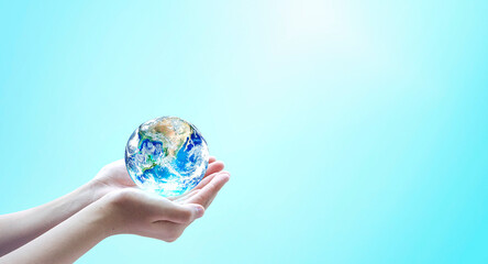 Human hands hold globe on blurred blue nature background. Elements of this image furnished by NASA