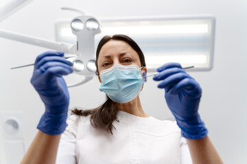 Fototapeta na wymiar Beautiful female dentist in a protective mask holds dental instruments in her hands, treats her patient's teeth. Professional work of a dentist in a dental clinic.