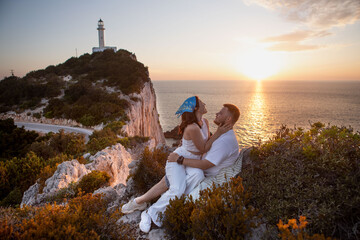 happy couple meeting sunset sitting on the cliff Lefkada lighthouse on the background