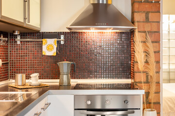 View of the kitchen with stovetop, sink and extractor hood with stylish burgundy mosaic tiles and white doors on the cabinets. Concept of stylish and comfortable kitchen interior