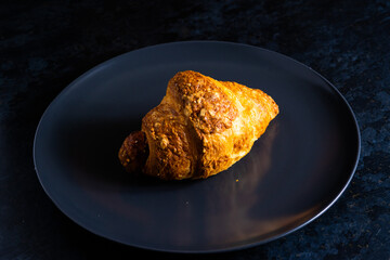 Freshly backed french croissant shiny in the rays of the morning sun, dark background, kitchen