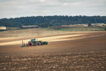 Tractor with seeder at work in field. Tractor with seed drill and power harrow working on field. Farmer driving tractor and drilling seed in ploughed field. Farmer seeding, sowing crops at field