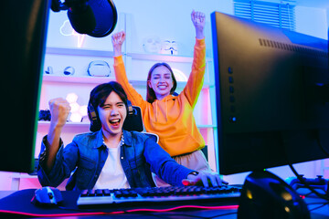 Asian male gamer and Caucasian woman coach celebrating victory together in front of the gaming...