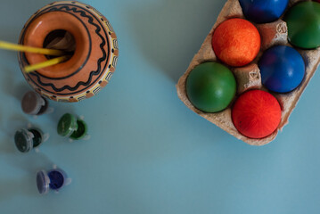 easter theme composition - coloured eggs, paint and brushes on blue background
