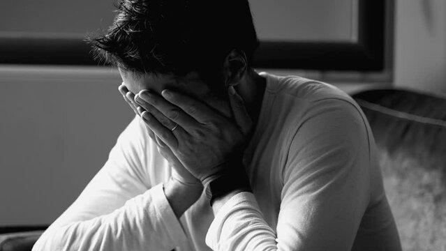 One depressed man suffering from mental illness covers face in regret. Male depression in monochromatic black and white