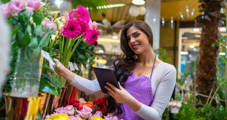 A young florist carefully checks the prices in the flower shop using a tablet
