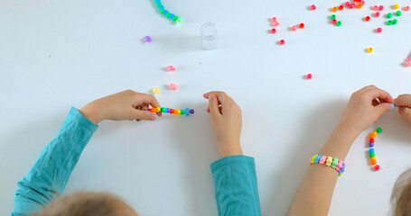 Little girls makes diy accessories bracelet from beads. Hobby for children