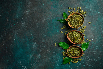 Peeled pumpkin seeds in a wooden bowl. On a dark textured background. Copy space.