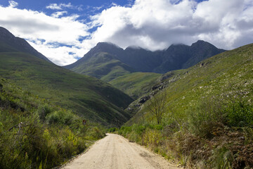 Dirt road leading to the mountains with blue sky and clouds ahead to explore.