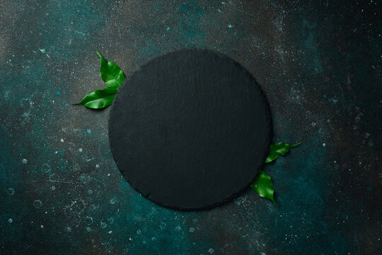 Round black slate plate. On a dark green-turquoise background. Free space for text.