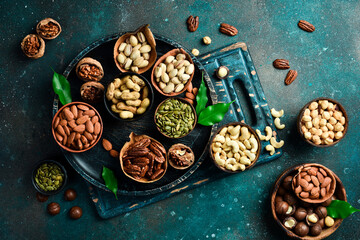 Peanuts, walnuts, almonds, hazelnuts and cashews mixed together in wooden bowls. Top view. On a dark background.