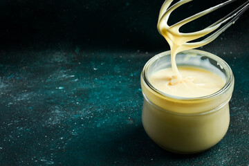 Glass jar with condensed milk. On a black background. Kitchen whisk.