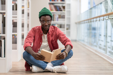 Interested Black student man sitting on floor in library. Focused African American guy preparing...