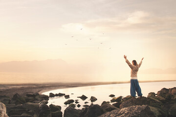 woman with arms outstretched takes a breath in front of a spectacular seascape - obrazy, fototapety, plakaty
