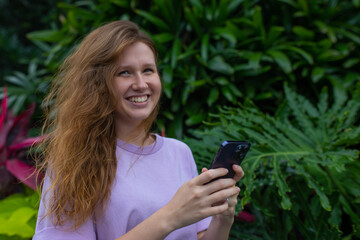 girl in the park or in nature uses a mobile phone, looks at the screen, smile and communication 