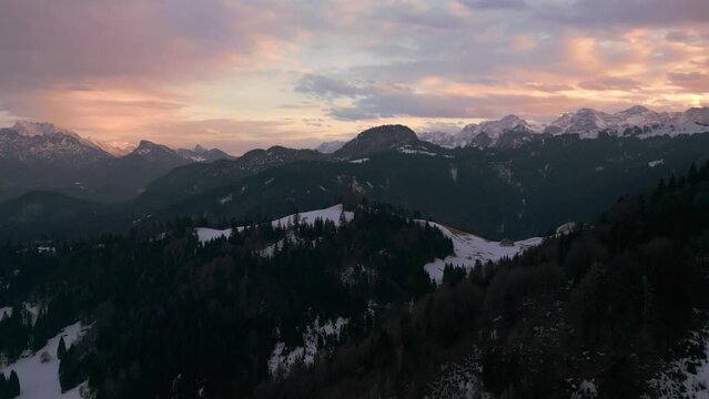 Mountain sunset in snowy landscape with forest, trees, snow and sunlight. Aerial drone view flying in cinematic alpine winter scenery in Austria Bavaria alps mountains valley. 4K UHD epic documentary.