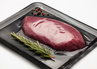 Fresh raw beef fillet steak sealed in vacuum tray with pepper and rosemary on white background.