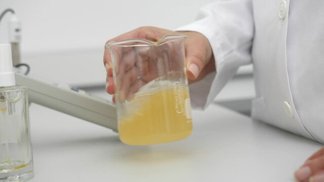 closeup of female scientist mixing yellow liquid in beaker in scientific lab slow motion