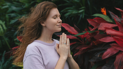 girl meditates in a park in nature or prays in a tropical garden, relaxes in nature and breathes...