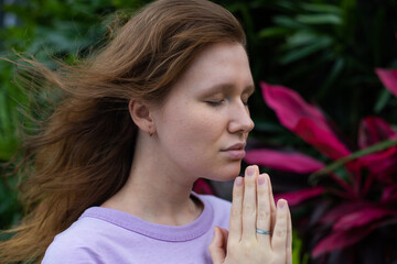 girl meditates in a park in nature or prays in a tropical garden, relaxes in nature and breathes...