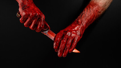 A man wipes a bloody knife with his hand on a black background.  © Михаил Решетников