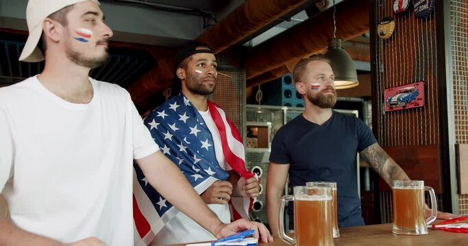 Fans watching football in a bar with friends, football, hockey, basketball, sports games. Friends at the bar in a pub having fun. Men with the flag of the national country of USA.