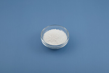 Sodium benzoate, sodium salt of benzoic acid in glass dish on blue background. Food additive E211. White granulated powder, chemical formula C6H5COONa