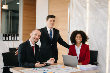 Happy businesspeople while collaborating on a new project in an office. Group of diverse businesspeople using a laptop and tablet in office..