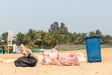 A dustbin and plastic bags full of trash on the beach in Sinquerim.