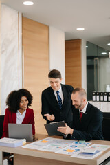 Happy businesspeople while collaborating on a new project in an office. Group of diverse businesspeople using a laptop and tablet in office..